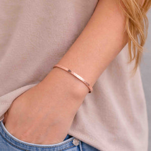 8 of 9: Close-up of a woman wearing a slim 3.5mm hand-hammered copper cuff bracelet on her wrist. The bracelet features a warm, polished copper finish with a lightly textured surface. Her hand is tucked into the pocket of light-wash denim jeans, and she is wearing a soft beige top. The overall look is casual and relaxed, highlighting the bracelet’s simple, handcrafted elegance.