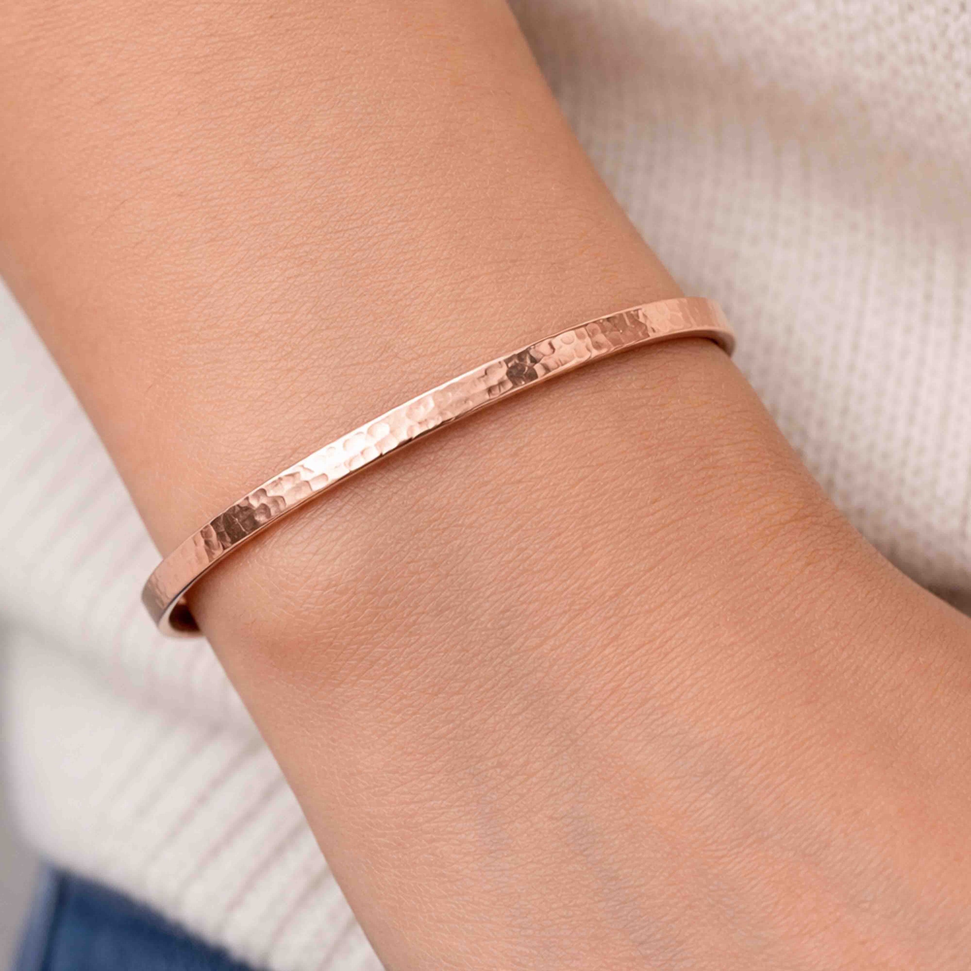 Close-up of a person wearing a 3.5mm Hammered Copper Cuff Bracelet on the wrist. The narrow open cuff features a warm polished finish and hand-hammered texture that reflects light across the surface. A soft cream knit top appears in the background, keeping attention on the minimalist handmade bracelet.