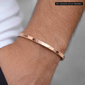 6 of 9: Close-up of a person’s wrist wearing a slim 3.5mm hand-hammered copper cuff bracelet. The raw copper surface shows a warm reddish shine with subtle hammered texture catching the light. The open-ended cuff fits snugly around the wrist for a minimalist look. A light sleeve edge appears near the wrist, and the background is softly blurred in neutral gray tones.  AI Generated Model.