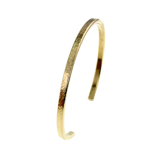 8 of 10: Slim hammered Nu Gold brass cuff bracelet shown at an angled side view against a clean white background. The narrow 3.5mm band features a lightly textured, hand-hammered surface that reflects warm golden tones, with smooth inner edges and gently rounded ends. The open cuff design highlights its simple, minimalist, handcrafted style.