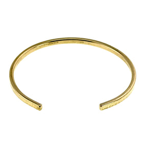 5 of 10: Slim hammered Nu Gold brass cuff bracelet shown from an overhead angle against a clean white background. The narrow 3.5mm band features a lightly textured, hand-hammered finish on the outer surface with a smooth inner side. The open cuff design has gently rounded ends, highlighting its minimalist, handcrafted style and warm golden tone.
