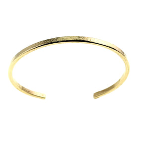 6 of 10: Slim hammered Nu Gold brass cuff bracelet shown at a slight angle against a clean white background. The narrow 3.5mm band features a softly textured, hand-hammered surface along the top with smooth edges and interior. The open cuff design includes gently rounded ends, highlighting its warm golden tone and simple, handcrafted style.