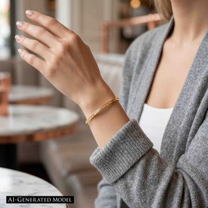 8 of 10: Close-up of a woman’s wrist wearing a slim 3.5mm linen bronze cuff bracelet with a soft hammered texture. The warm golden tone complements a casual outfit with a gray knit sweater and white top, set against a softly blurred indoor background with neutral tones.  AI Generated Model.