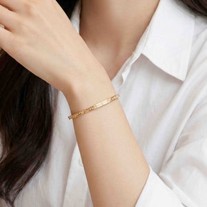 8 of 10: Close-up of a woman’s wrist wearing a slim 3.5mm linen bronze cuff bracelet with a subtle hand-hammered texture. The warm golden tone pairs elegantly with a crisp white blouse, creating a clean and refined look with soft, natural lighting.