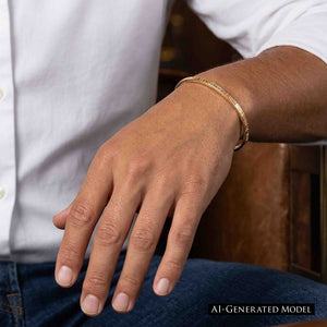 4 of 10: Close-up of a man’s wrist wearing a slim 3.5mm linen bronze cuff bracelet with a subtle hammered texture. The warm golden tone contrasts softly against the skin, styled with a white shirt and blue jeans for a casual, everyday look.  AI Generated Model.