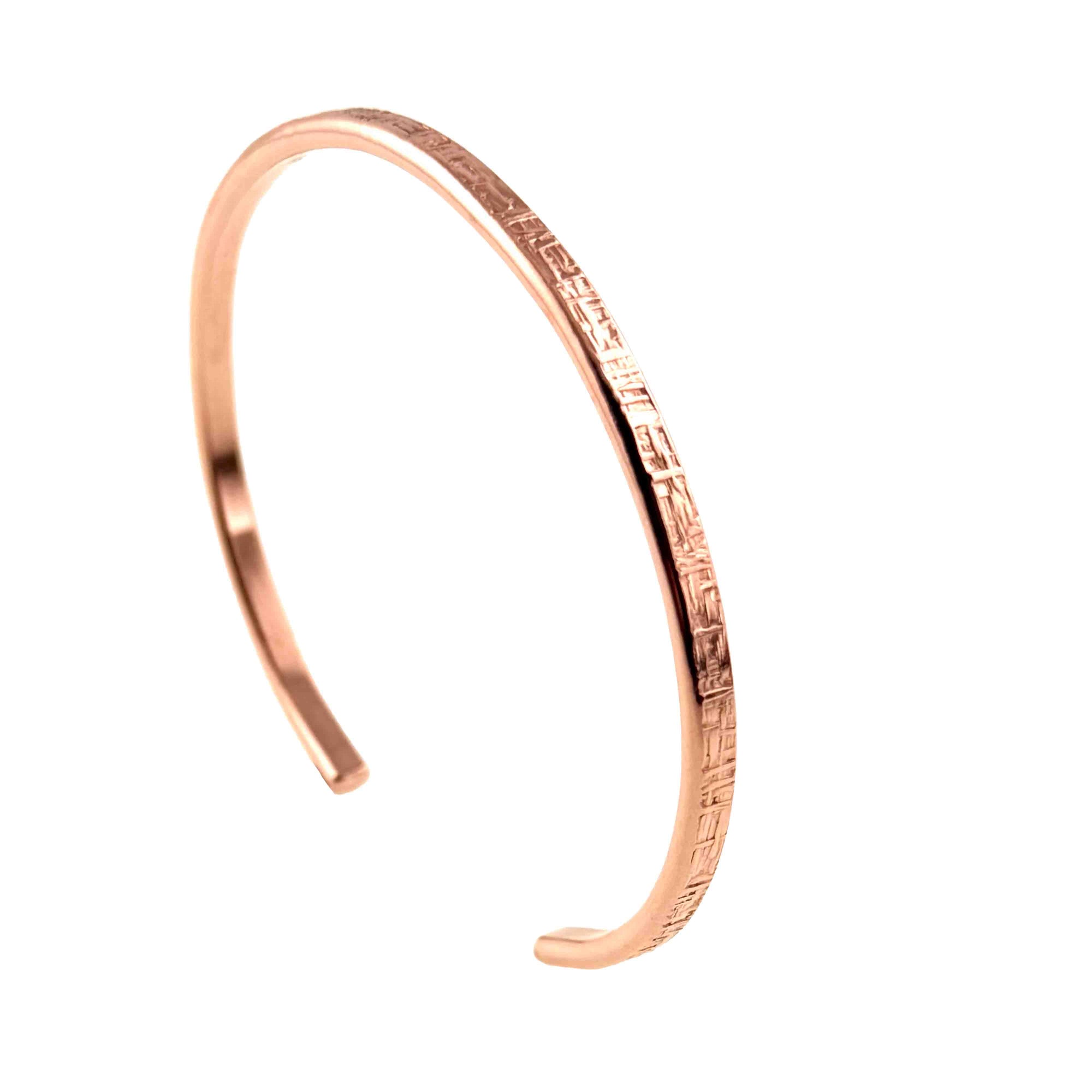 Slim 3.5mm solid copper cuff bracelet with a hand-applied linen texture displayed on a clean white background. The open cuff features a narrow profile, smooth polished edges, rounded ends, and a warm rose-copper finish. Shown at a slight angle, the textured outer surface highlights the handcrafted crosshatch pattern while the polished interior reflects light, emphasizing its minimalist artisan design.