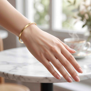 8 of 9: Matte bronze cuff bracelet worn on a woman’s wrist near a marble table and coffee cup. The slim handcrafted bronze bracelet features a brushed satin finish and simple open cuff design that works beautifully with relaxed daytime fashion and layered jewelry looks.