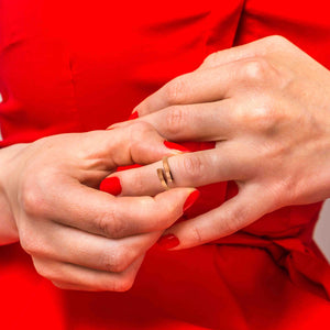 4 of 10: A woman in a red dress with matching red nail polish gently placing a 3.5mm matte copper bypass ring on her finger.