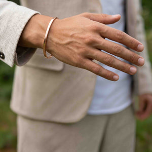 2 of 10: Matte copper cuff bracelet worn on a man’s wrist with a light jacket, showing its slim unisex style, warm copper finish, and easy casual look.