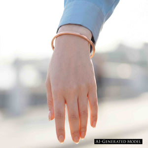 4 of 10: Slim copper cuff bracelet worn on a woman’s wrist with a blue sleeve, highlighting the simple open cuff design, warm shine, and light everyday fit.  AI Generated Model.
