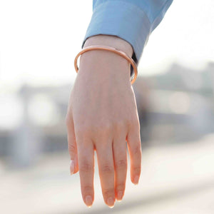 6 of 10: Slim copper cuff bracelet worn on a woman’s wrist with a blue sleeve, highlighting the simple open cuff design, warm shine, and light everyday fit.