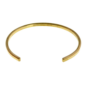 5 of 10: Top view of a slim 3.5mm matte Nu Gold brass cuff bracelet on a white background, showing its oval shape, open ends, softly brushed golden surface, and faint John S. Brana maker’s mark inside the band.
