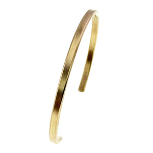 3 of 10: Angled side view of a narrow matte Nu Gold brass cuff bracelet on a white background, showing the slim rectangular profile, rounded curve, open design, and softly finished ends.