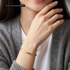 2 of 10: AI generated female model wearing a slim matte Nu Gold brass cuff bracelet with a gray cardigan and white top, shown in a close view that draws attention to the bracelet on her wrist.