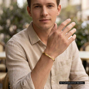 8 of 10: AI generated male model in a beige button front shirt wearing a slim matte Nu Gold brass cuff bracelet on his wrist while seated in a softly blurred outdoor café setting.