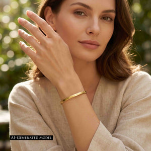 6 of 10: AI generated female model in a beige linen top wearing a slim matte Nu Gold brass cuff bracelet on her raised wrist, with soft sunlight and blurred green foliage in the background.