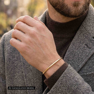 4 of 10: A bearded man wearing a gray herringbone coat and dark brown knit top holds one hand near his chest. A narrow polished bronze cuff bracelet circles his wrist and adds a warm golden accent to the cool gray clothing. A label reads “AI GENERATED MODEL.”