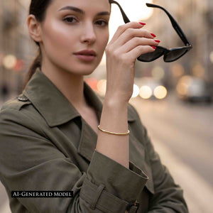 8 of 10: A woman in an olive green jacket holds black sunglasses near her face on a softly blurred city street. Her red manicure draws attention to the narrow polished bronze cuff bracelet around her raised wrist. A label reads “AI GENERATED MODEL.”