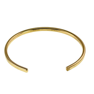 7 of 11: Low angle product view of a narrow polished Nu Gold brass cuff bracelet on a white background. The open ends face forward, and the curved golden band shows its flat outer surface, smooth edges, and reflective finish.