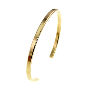 10 of 11: Side angle view of a narrow Nu Gold brass cuff bracelet standing upright on a white background. The polished golden band curves into an open oval and shows its slim 3.5mm width, smooth edges, and reflective surface.