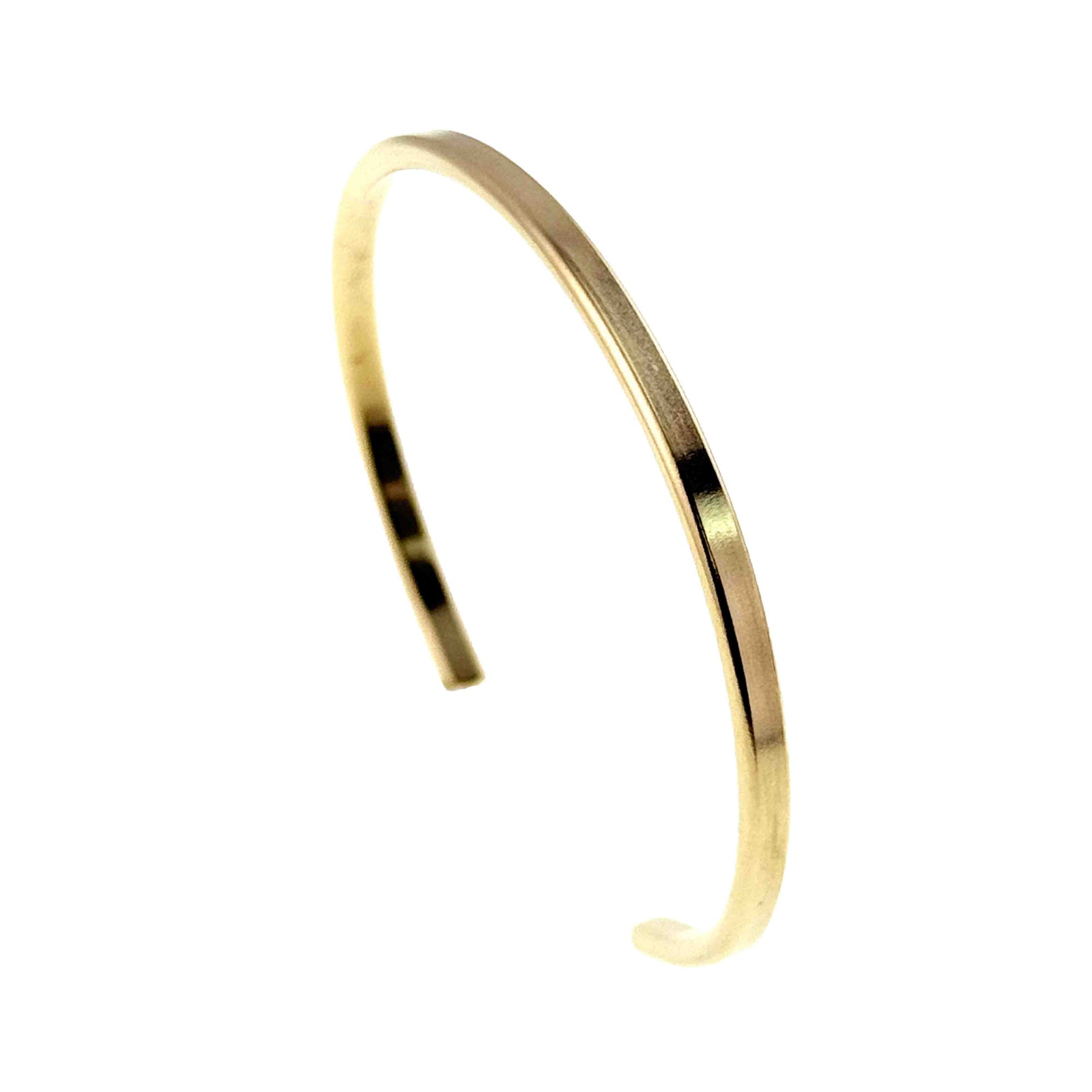 Opposite side angle view of a slim polished Nu Gold brass cuff bracelet standing upright on a white background. Light reflects along the smooth golden band, highlighting its narrow shape, curved profile, and open ends.