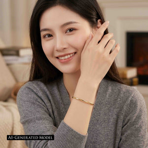 8 of 11: Smiling woman wearing a narrow polished golden brass cuff bracelet with a gray sweater in a warm indoor setting. Her raised hand frames her face while the bracelet rests clearly on her wrist. A black label reads AI generated model.
