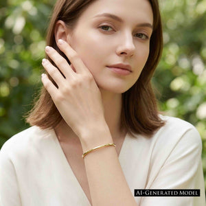 2 of 11: Woman wearing a slim polished golden brass cuff bracelet with a cream blouse in a softly lit garden setting. She raises one hand near her face, keeping the bracelet visible on her wrist. A black label reads AI generated model.