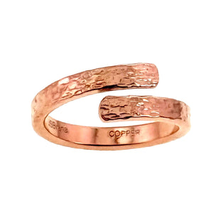 5 of 9: Rear view of the open copper bypass ring on a white background. The smooth polished interior shows the John S. Brana maker mark and COPPER stamp, while the outer band has a hand applied texturized surface.