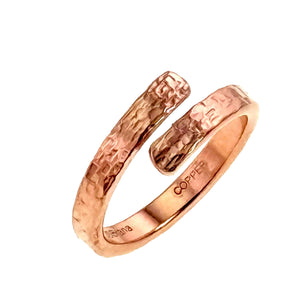 7 of 9: Angled close view of the polished copper bypass ring on a white background. Two rounded ends overlap with an open space between them, showing the hand applied texture across the warm copper surface.