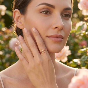 6 of 9: Woman posing in a sunlit garden while wearing the texturized copper bypass ring. Her hand rests near her face, showing the two open textured ends of the warm polished copper band.