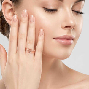 2 of 9: Close view of a woman with closed eyes touching her cheek while wearing a polished copper bypass ring. The slim ring wraps around her finger with two open ends and a hand applied texturized finish.