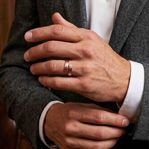 8 of 9: Close view of a man seated in a gray suit and white shirt wearing the texturized copper bypass ring. The slim open ring adds a warm copper accent to his tailored business clothing.