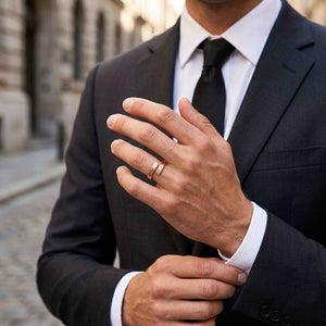 4 of 9: Man in a dark suit, white shirt, and black tie wearing a polished copper bypass ring outdoors. His raised hand displays the slim texturized ring against a softly blurred city background.