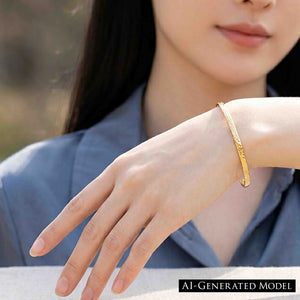 7 of 9: A woman in a slate blue blazer models a slim golden Nu Gold brass cuff bracelet on her extended wrist. The close view shows the bracelet’s narrow 3.5mm shape, polished edges, hand applied texture, and open cuff ends against a softly blurred indoor background. AI Generated Model.