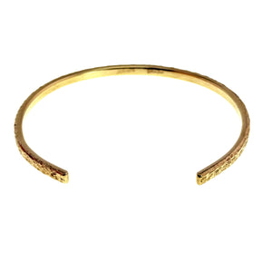 8 of 9: Angled overhead product view of a slim Nu Gold brass cuff bracelet on a white background. The opening faces forward, revealing two smooth squared ends, a polished inner surface, and a hand textured golden exterior that follows the bracelet’s curved shape.