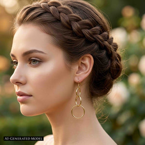 2 of 8: AI generated woman with brunette hair styled in a braided updo wearing a 3 Tiered Hammered Nu Gold Brass Chandelier Earring outdoors, showing the long open circle design hanging below the jaw and the polished golden finish against a softly blurred garden background.