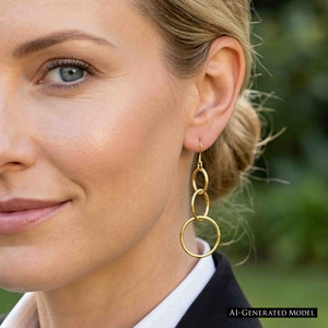 7 of 8: Close up view of an AI generated blonde woman wearing a 3 Tiered Hammered Nu Gold Brass Chandelier Earring with her hair pulled back, showing the approximately 3 inch drop, graduated round links, and warm golden finish against a softly blurred green outdoor setting.