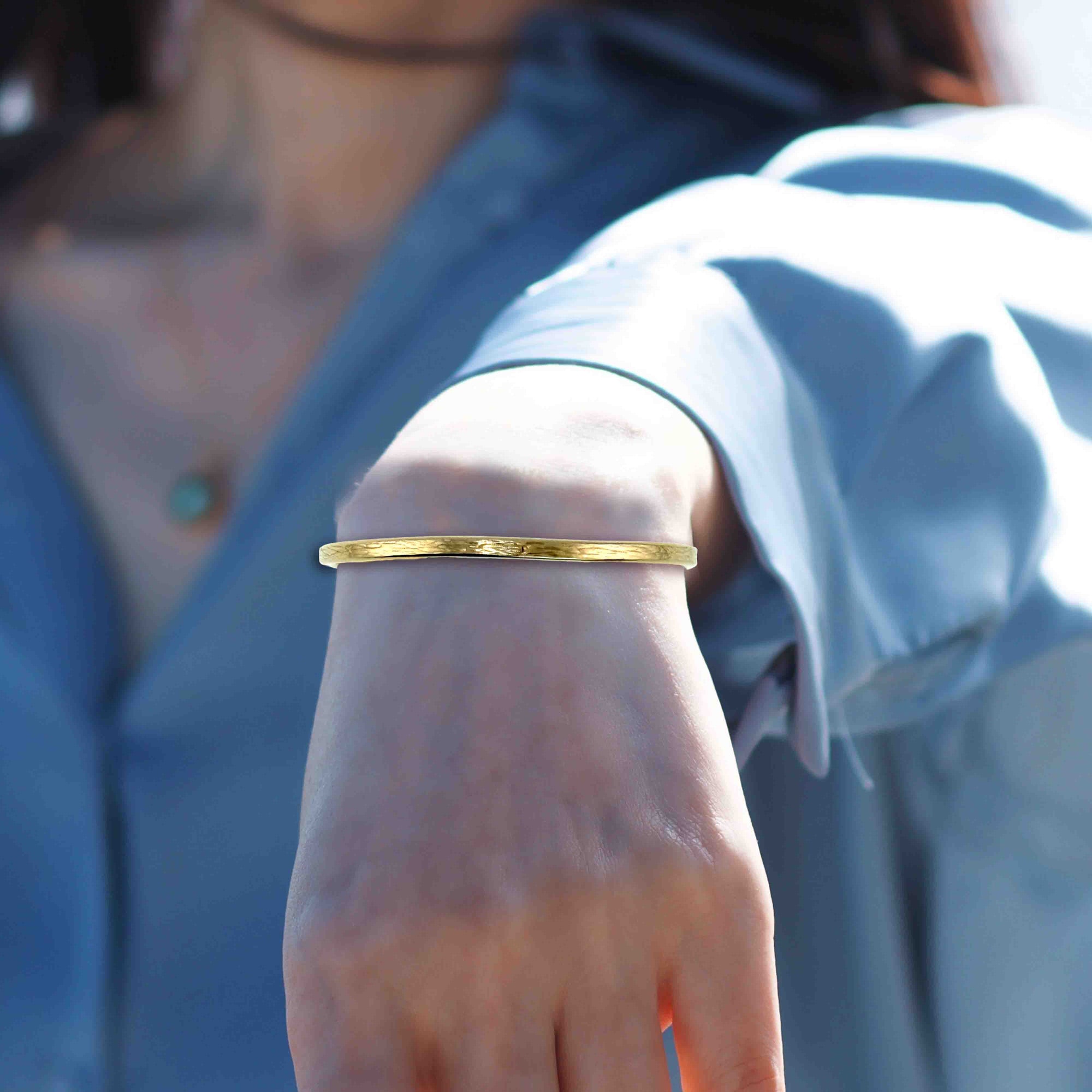 3.5mm Bark Nu Gold Brass Cuff Bracelet on a Woman's wrist with a blurred background