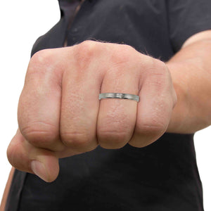 7 of 10: A close-up image of a man’s clenched fist, showcasing a slim stainless steel ring with a bark-textured finish worn on the ring finger. The man is wearing a dark short-sleeve shirt, and the plain white background keeps the focus on the ring’s natural, hand-carved design.