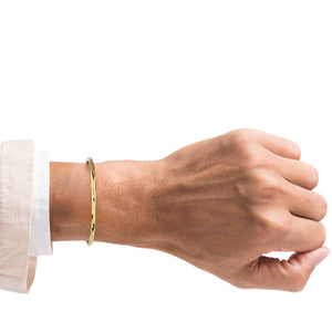 2 of 8: A Man's hand wearing a 3mm Hammered Solid Nu Gold Brass Cuff Bracelet on a white background