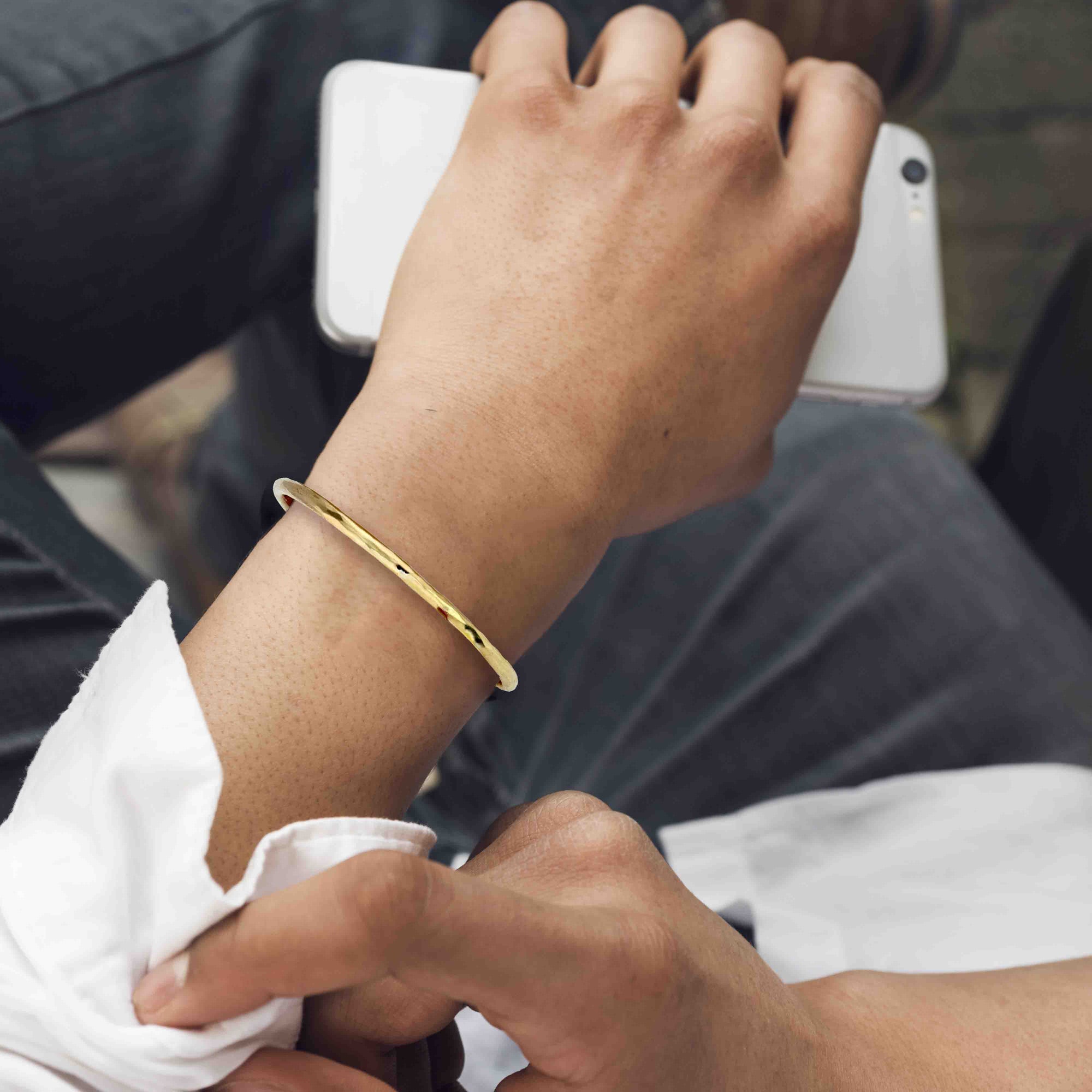 Close-up of a person's wrist wearing a 3mm Hammered Solid Nu Gold Brass Cuff Bracelet with a blurred background.