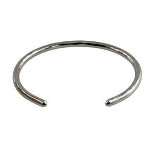 7 of 10: Angled product photograph of the 3mm Hammered Stainless Steel Cuff Bracelet by John S. Brana on a white background, showing its open cuff construction and rounded ends. Made from solid 316L surgical stainless steel, the bracelet features a hand hammered texture that reflects light along its narrow silver tone surface. The photograph highlights the bracelet's oval curvature and the opening that allows it to slide onto the wrist.
