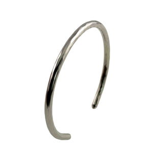 3 of 10: Three-quarter side view of the 3mm Hammered Stainless Steel Cuff Bracelet by John S. Brana against a white background. The handcrafted 316L surgical stainless steel bracelet is positioned at an angle to reveal its curved profile, open ends, and slender rounded construction. Light reflects across the hand hammered surface, showing the irregular texture and polished silver tone of this minimalist metal cuff.