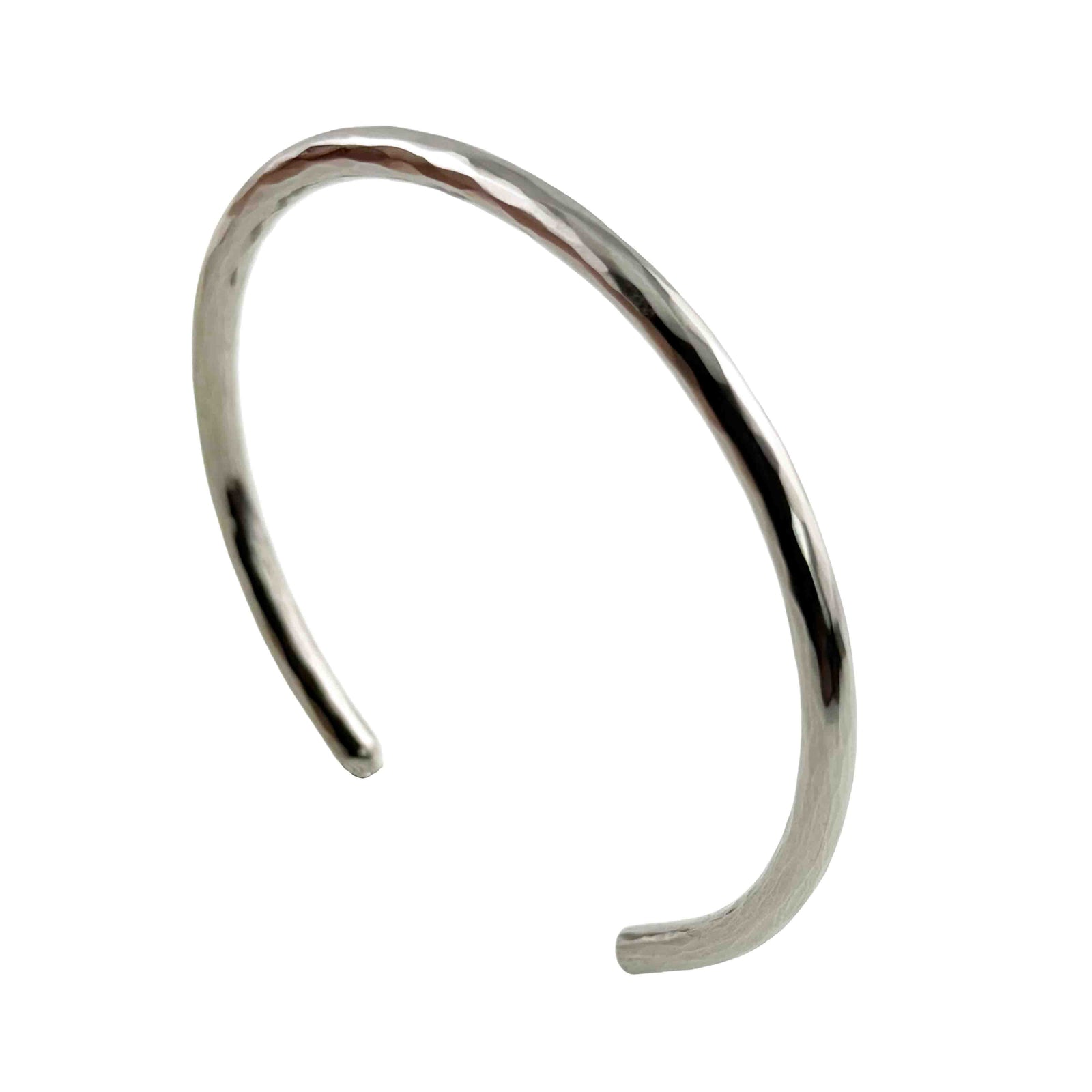 Main product photograph of the 3mm Hammered Stainless Steel Cuff Bracelet by John S. Brana displayed at a three-quarter angle against a pure white background. Handcrafted from solid 316L surgical stainless steel, the slim bracelet features a bright silver tone, hand hammered surface, smooth rounded edges, and an open cuff design. The angled view highlights the bracelet's elegant curved shape, textured metalwork, and minimalist styling for women and men.
