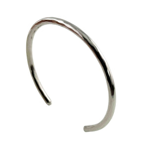 1 of 10: Main product photograph of the 3mm Hammered Stainless Steel Cuff Bracelet by John S. Brana displayed at a three-quarter angle against a pure white background. Handcrafted from solid 316L surgical stainless steel, the slim bracelet features a bright silver tone, hand hammered surface, smooth rounded edges, and an open cuff design. The angled view highlights the bracelet's elegant curved shape, textured metalwork, and minimalist styling for women and men.