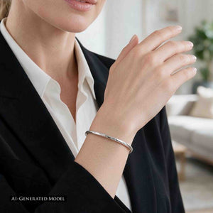 8 of 10: AI-generated female model wearing a 3mm Hammered Stainless Steel Cuff Bracelet by John S. Brana with a tailored black blazer and white blouse. The narrow, handcrafted 316L surgical stainless steel bracelet features a bright silver tone, subtle hand hammered texture, and sleek minimalist design. Shown on her wrist in a softly lit interior, the cuff provides an understated jewelry accent for professional and everyday fashion.