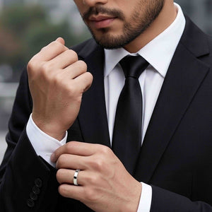 8 of 9: Close up of a man in a black suit, white dress shirt, and black tie adjusting his cuff while wearing a polished stainless steel flat band ring. The slim silver ring has a narrow width, flat profile, and bright reflective finish that adds a clean modern accent to his formal look. Its simple unisex style suits everyday wear, weddings, engagements, anniversary gifts, or polished professional styling.