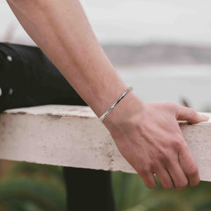 5 of 9: A man's wrist wearing a 4.75mm Hammered Aluminum Cuff Bracelet blurred background