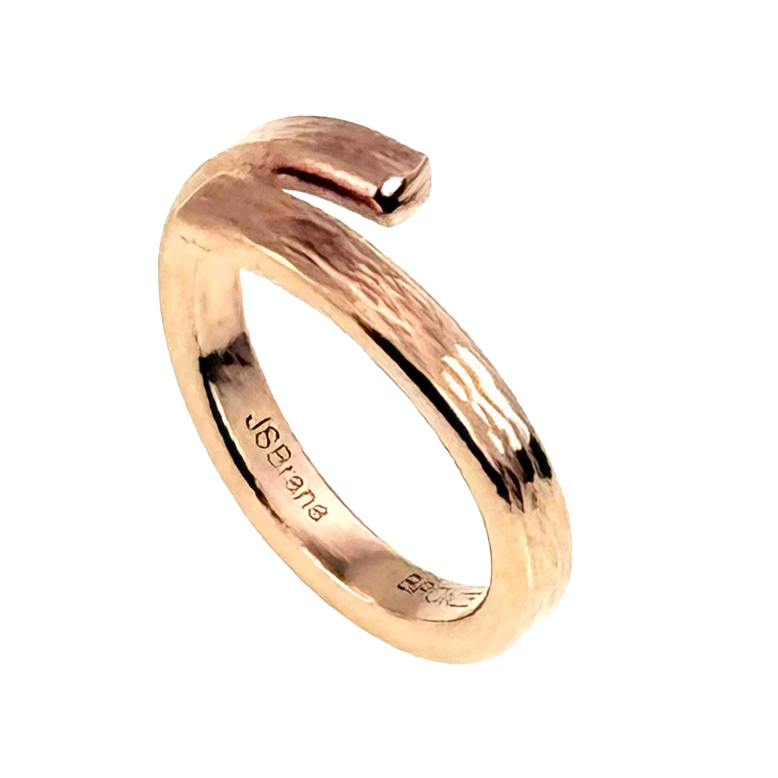 Handcrafted bronze bypass ring shown on a white background. The slim ring has an open wrap design with one end crossing slightly over the other, creating a modern bypass shape. Its warm golden bronze surface features a subtle bark like texture with polished highlights. The inside of the band is stamped “JSB bronze,” showing the maker’s mark.