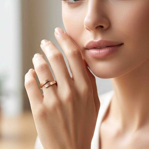 6 of 9: Close up of a woman’s face and hand wearing a slim bronze bypass ring on her finger. The open band wraps around with two flat ends that nearly meet, showing a fine bark texture and warm polished bronze finish. Her hand rests near her cheek in soft natural light, creating an elegant, minimal styling image that highlights the ring’s modern, handcrafted look.